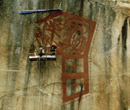 Two people on a scaffold, painting the design on the cliff